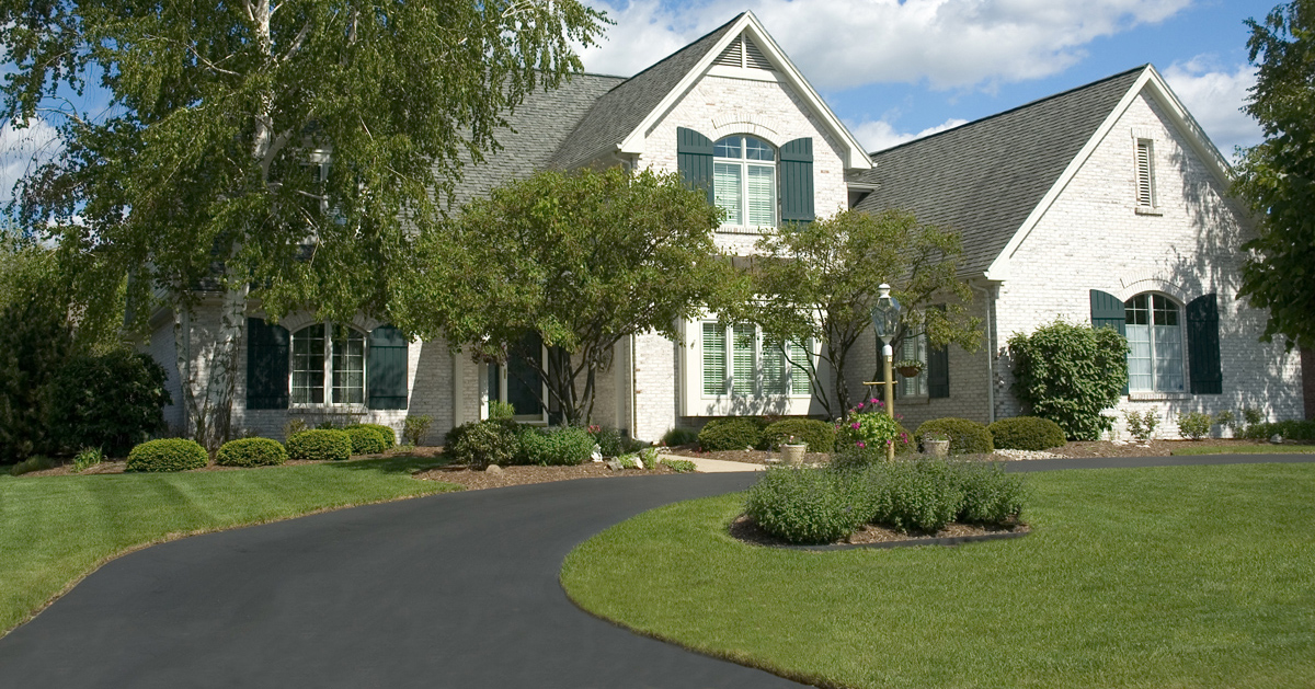 Large white house with well landscaped yard and new, black driveway across the front of the house.